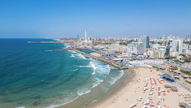 A coastal cityscape with a beach, buildings, and a prominent lighthouse.
