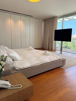 A modern hotel room with a large bed, a flat-screen TV, a wooden bedside table with a phone, and a view of the outdoors through large windows. - Carmelo  Treasure Villa (Herzliya)