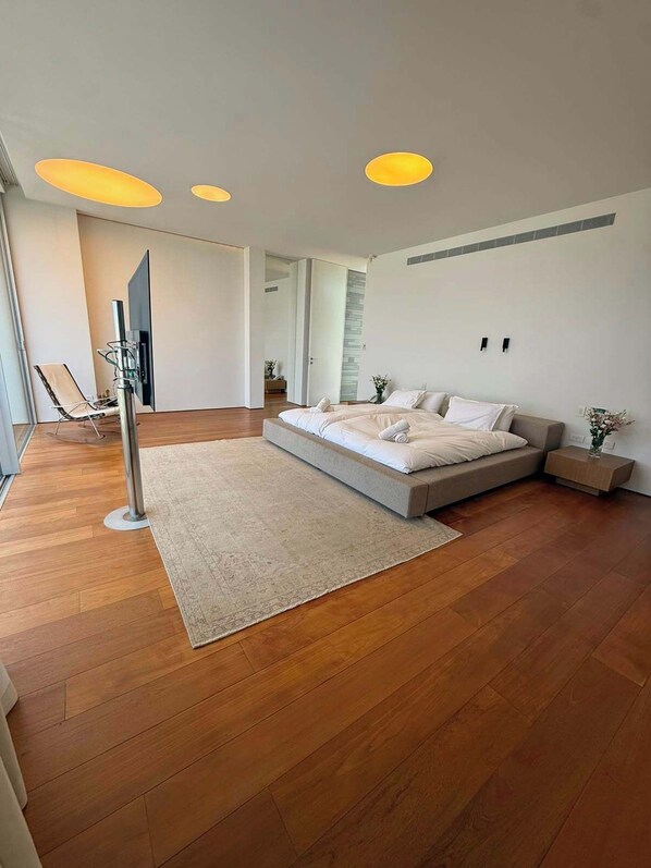 A modern bedroom with a large bed, a standing lamp, and a view of the hallway.