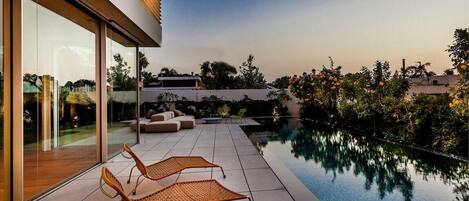 Un área de piscina moderna al aire libre con sillones de descanso y un porche con paredes de vidrio.