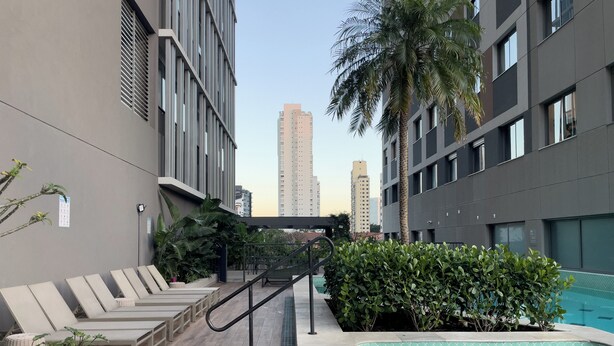 Un área moderna de piscina al aire libre con sillones reclinables, una escalera y vistas de edificios altos circundantes.