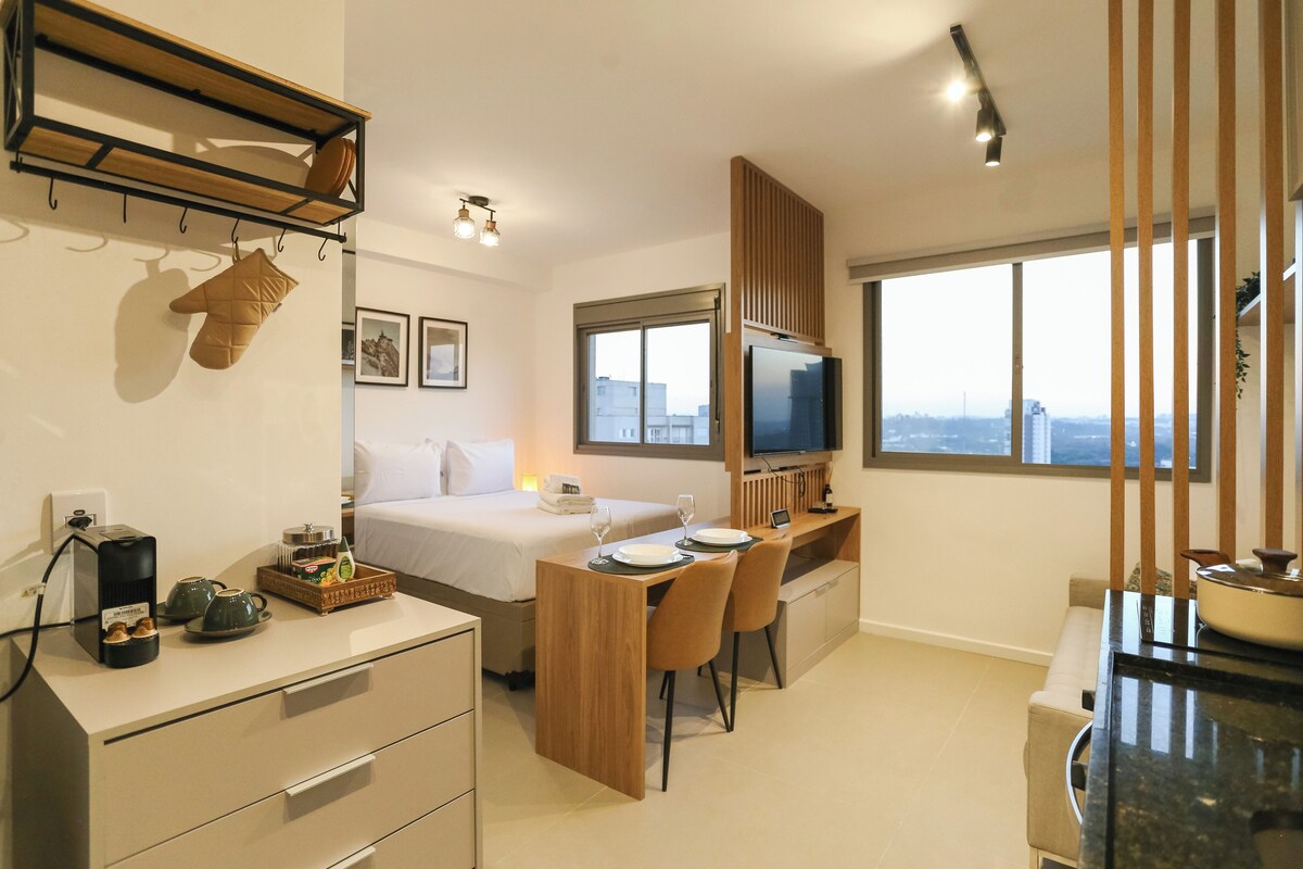 A modern hotel room with a bed, a desk, a TV, and a large window with a city view.