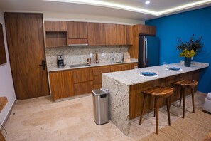 Une cuisine moderne avec des meubles en bois, des plans de travail en granit, un réfrigérateur en acier inoxydable et des tabourets de bar.