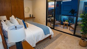 Une chambre à coucher avec un lit, une lampe de chevet et une vue sur un balcon aménagé avec des sièges d’extérieur.