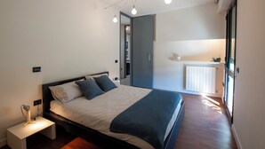 A modern bedroom with a bed, bedside table, and a view of a kitchen area.