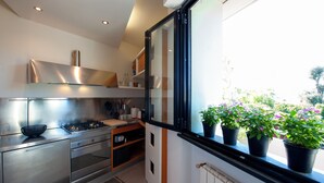 A modern kitchen with stainless steel appliances, a window with potted plants, and a view of greenery outside.