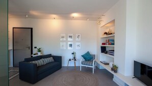 A modern living room with a dark blue sofa, a round woven rug, a white armchair, and a TV on a white stand.