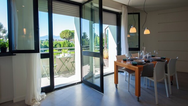 A modern dining area with a wooden table and chairs, large sliding glass doors leading to a balcony, and pendant lighting.