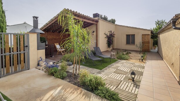 Een terras met een pergola, zitplaatsen buiten en een kleine tuin.
