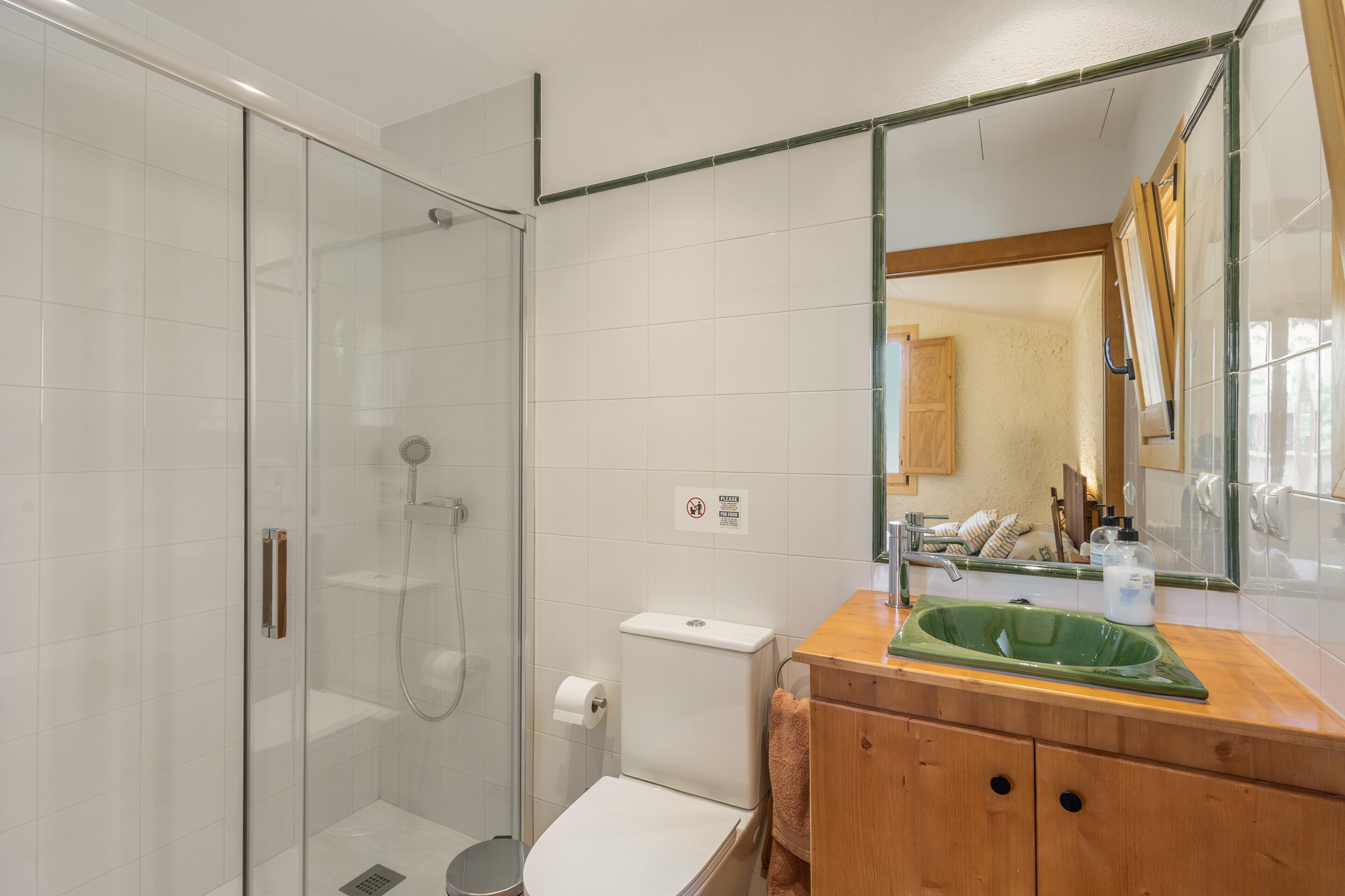 A bathroom with a glass-enclosed shower, a toilet, and a sink with a mirror above it.
