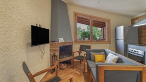 Een zithoek met een open haard, een bank, een televisie en een keuken met een koelkast.