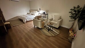 A bedroom with a bed, two chairs, a small table, a bedside lamp, and a nightstand. - Cozy room in lovely with side yard in Riyadh with WiF (Riyadh)