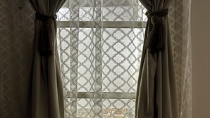 A room with a large window covered by patterned curtains, a wooden floor, and a patterned wall. - Cozy room in lovely with side yard in Riyadh with WiF (Riyadh)