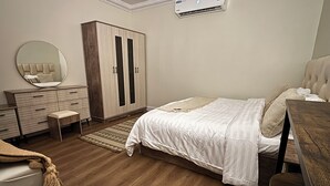 A bedroom with a bed, a wardrobe, a mirror, a bench, and an air conditioning unit. - Cozy room in lovely with side yard in Riyadh with WiF (Riyadh)