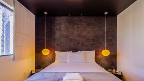 Een moderne hotelkamer met een groot bed, twee bedlampjes en een uitzicht op een stadslandschap door een raam.
