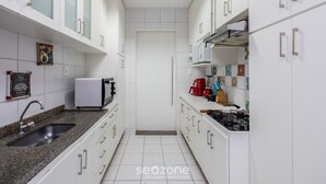 Een smalle keuken met witte kasten, een granieten aanrecht, een spoelbak, een magnetron, een kookplaat en een koffiezetapparaat.