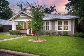Une maison d’habitation avec un porche à l’avant, un petit arbre et une pelouse bien entretenue.