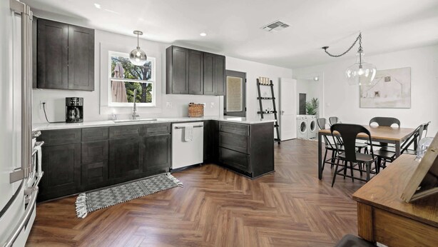 Une cuisine moderne avec des meubles de couleur sombre, un îlot central et un coin repas comprenant une table et des chaises.