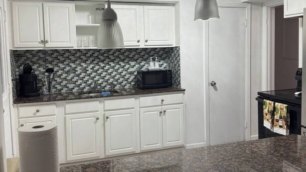 Una cocina con armarios blancos, salpicadero de azulejos, encimeras de granito e iluminación colgante.