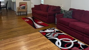 Un amplio salón con dos sofás rojos, suelo de madera y ventilador de techo.