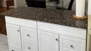 Una cocina con encimera de granito, armarios blancos e iluminación colgante.