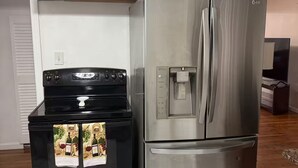Una cocina con estufa negra, refrigerador de acero inoxidable y alacenas blancas.