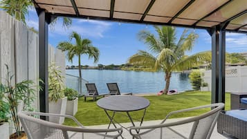 En overdækket terrasse med udsigt til en pool og palmer.