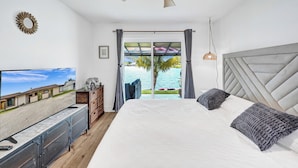 Une chambre avec un lit, une télévision, un ventilateur de plafond et une vue sur une piscine et des palmiers.