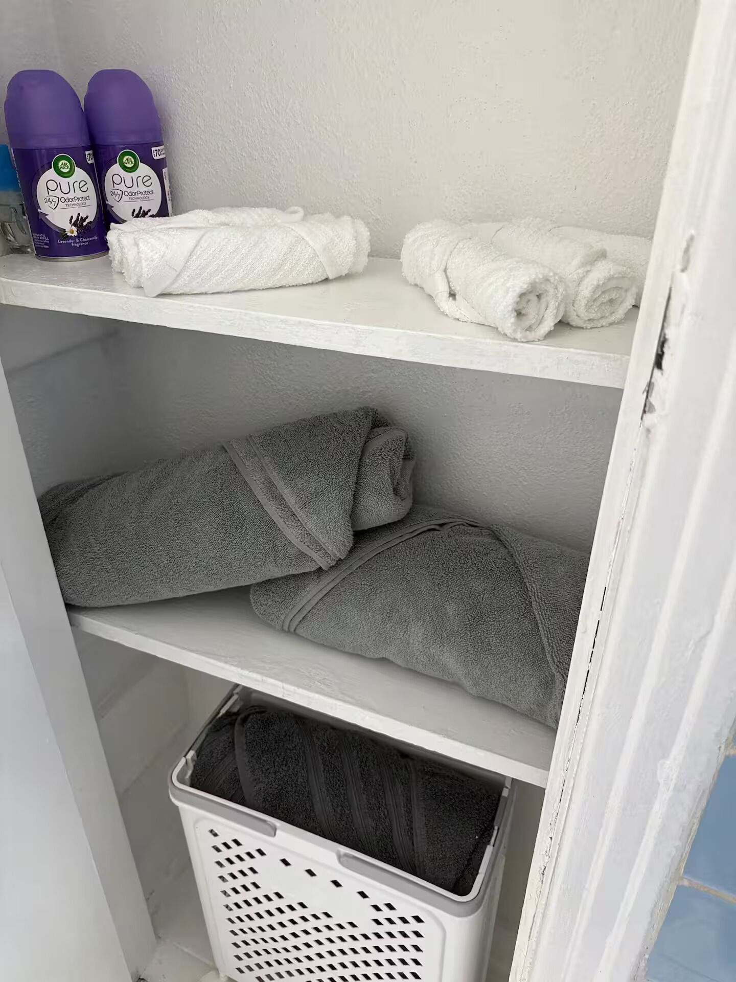 Een opbergruimte met planken vol opgevouwen handdoeken en een wasmand.