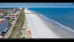 An aerial view of a beach with a pier extending into the ocean, buildings along the shore, and a clear sky. - Casa confortable y de descanso. (Jacksonville)
