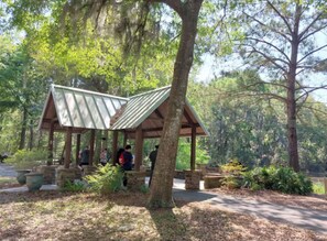 Un pavillon en bois doté d’un toit incliné, entouré d’arbres et bordé d’un chemin de gravier.