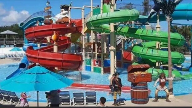 A water park with multiple water slides, including red and green ones, and a pool area with lounge chairs. - Casa confortable y de descanso. (Jacksonville)