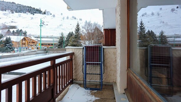 A balcony with a wooden railing, a metal gate, and a view of a snowy landscape with buildings and trees. - travelski home classic - Résidence Meijotel - Studio 4 personnes coin montagne L (Les Deux Alpes)