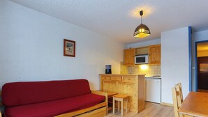 A compact living space with a red sofa, wooden dining table, and kitchenette. - travelski home classic - Résidence Meijotel - Studio 4 personnes coin montagne L (Les Deux Alpes)