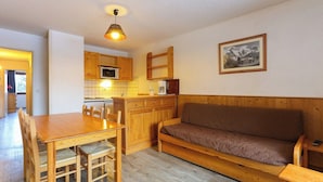Ein gemütliches Zimmer mit einem Holztisch, Stühlen, einer Couch und einer Küchenzeile mit Holzschränken und einer Mikrowelle.