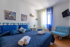 Um quarto com uma cama, uma cadeira, uma televisão e obras de arte na parede.