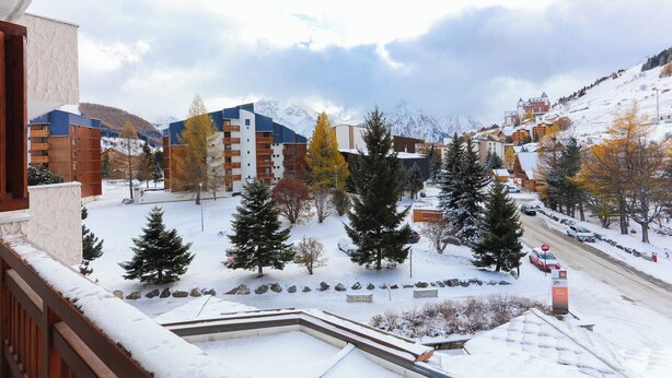 Una zona residencial nevada con edificios de varios pisos, una calle y montañas al fondo.