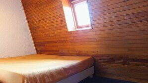 Una habitación pequeña con pared de madera, una cama individual y un ventanal.