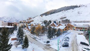 Estación de esquí nevada con chalets de madera, un edificio principal y un aparcamiento.