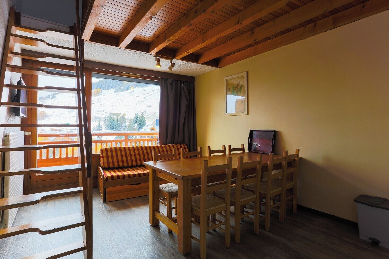 A cozy room with a wooden dining table, a sofa, and a view of a snowy mountain.