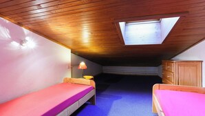 Una habitación pequeña y acogedora con dos literas de madera, un tragaluz y una alfombra azul.