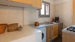 A compact kitchen with wooden cabinets, a washing machine, a coffee maker, and a window. - Terrazza al Poggio Vista Mare by Wonderful Italy (Olbia)