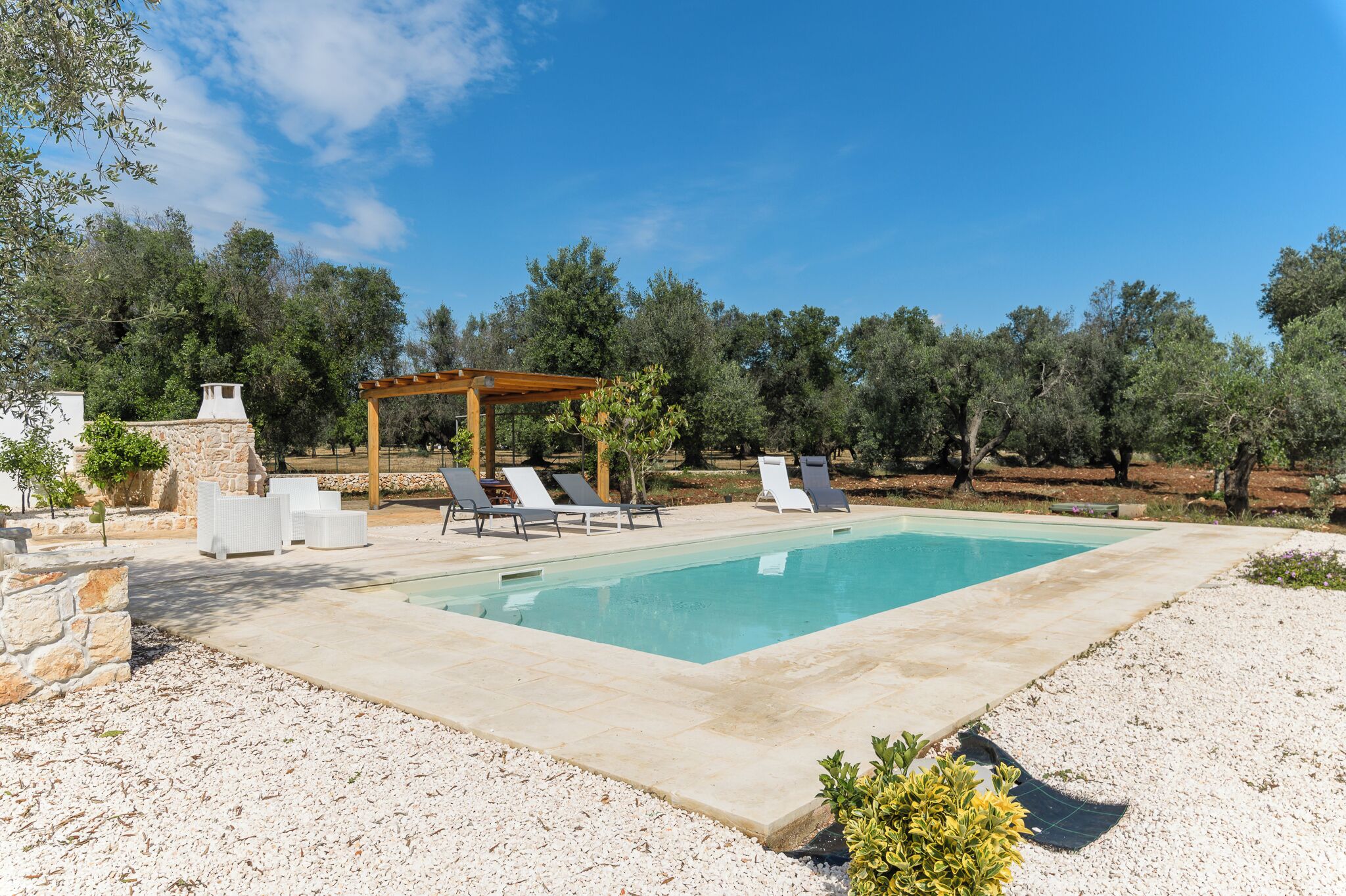 A swimming pool with lounge chairs, a pergola, and stone walls.