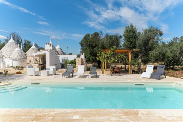 A swimming pool with lounge chairs, stone buildings with conical roofs, and a pergola. - Trulli Isabella by Wonderful Italy (Ceglie Messapica)