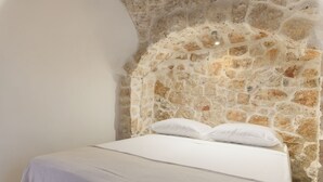 A bedroom with a stone wall and a bed with white linens. - Trulli Isabella by Wonderful Italy (Ceglie Messapica)