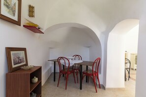 A dining area with a table and chairs, a wooden cabinet with a picture, and a shelf with decorative items. - Trulli Isabella by Wonderful Italy (Ceglie Messapica)