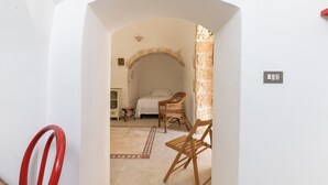 A bedroom with a bed, a wicker chair, and a small table. - Trulli Isabella by Wonderful Italy (Ceglie Messapica)