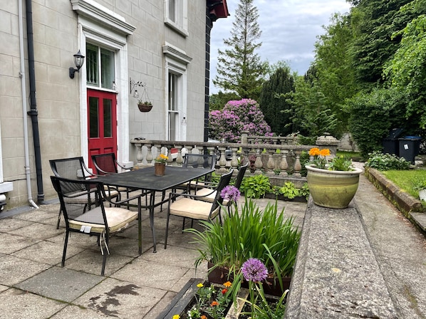 Un patio exterior con una mesa y sillas, rodeado de macetas con plantas y flores.