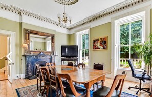 Comedor con mesa de madera, sillas, chimenea, televisor y ventana grande con vista a follaje.