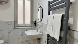A bathroom with a marble wall, a white sink, a toilet, and a towel rack with a towel. - Caltur B&B (Palermo)
